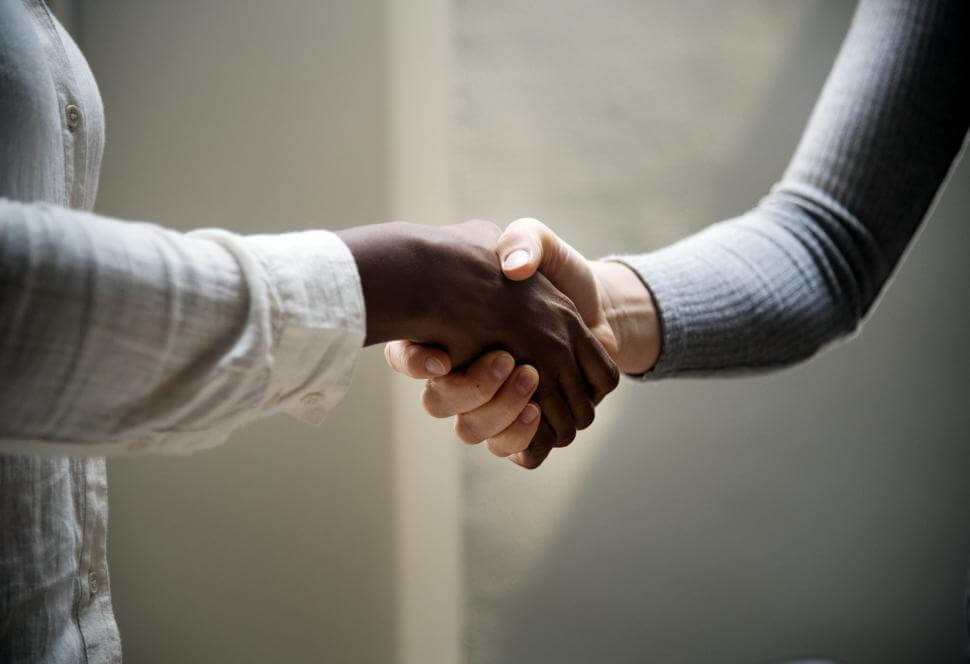 A photo of two people's arms shaking hands, zoomed in to only see the arms.